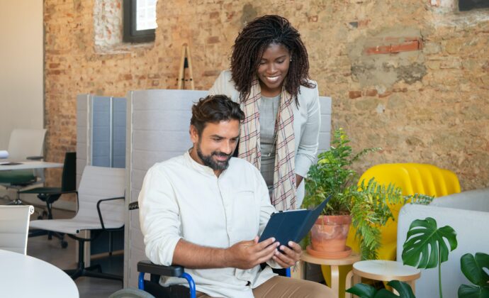 A man using a wheelchair and a woman smile at an iPad screen